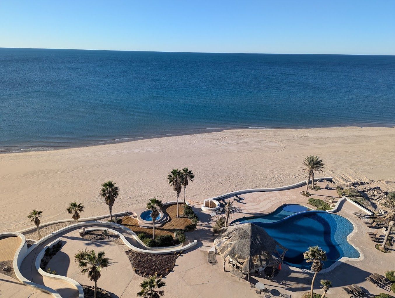 Beachfront resort pool and sandy shore beside a calm blue ocean under clear sky