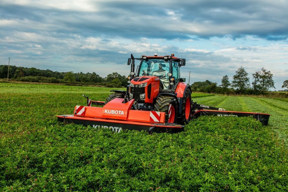 Ein roter Kubota-Traktor mäht unter bewölktem Himmel ein grünes Feld.