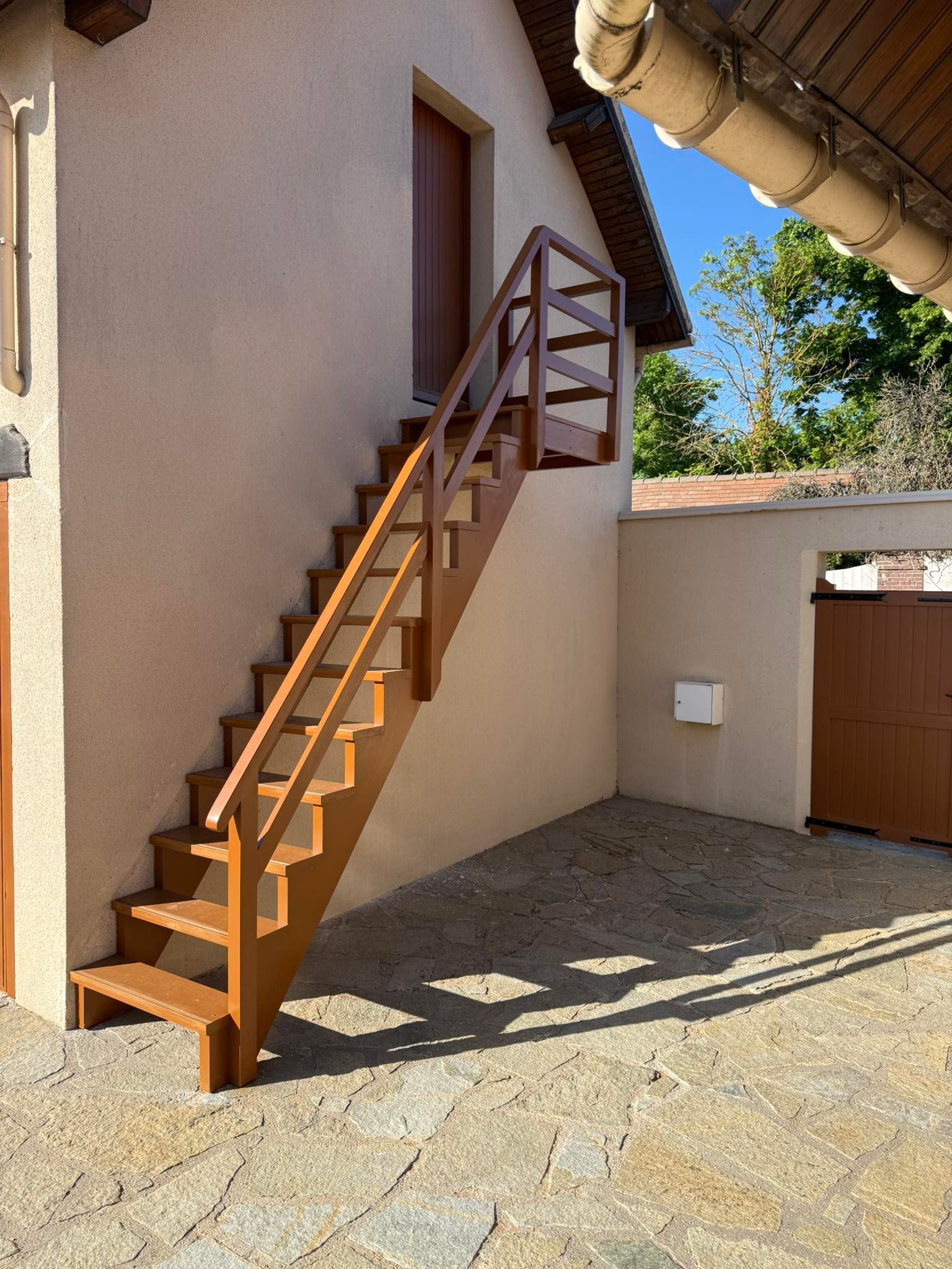 Un escalier extérieur en bois mène à une porte sur un bâtiment en stuc beige.