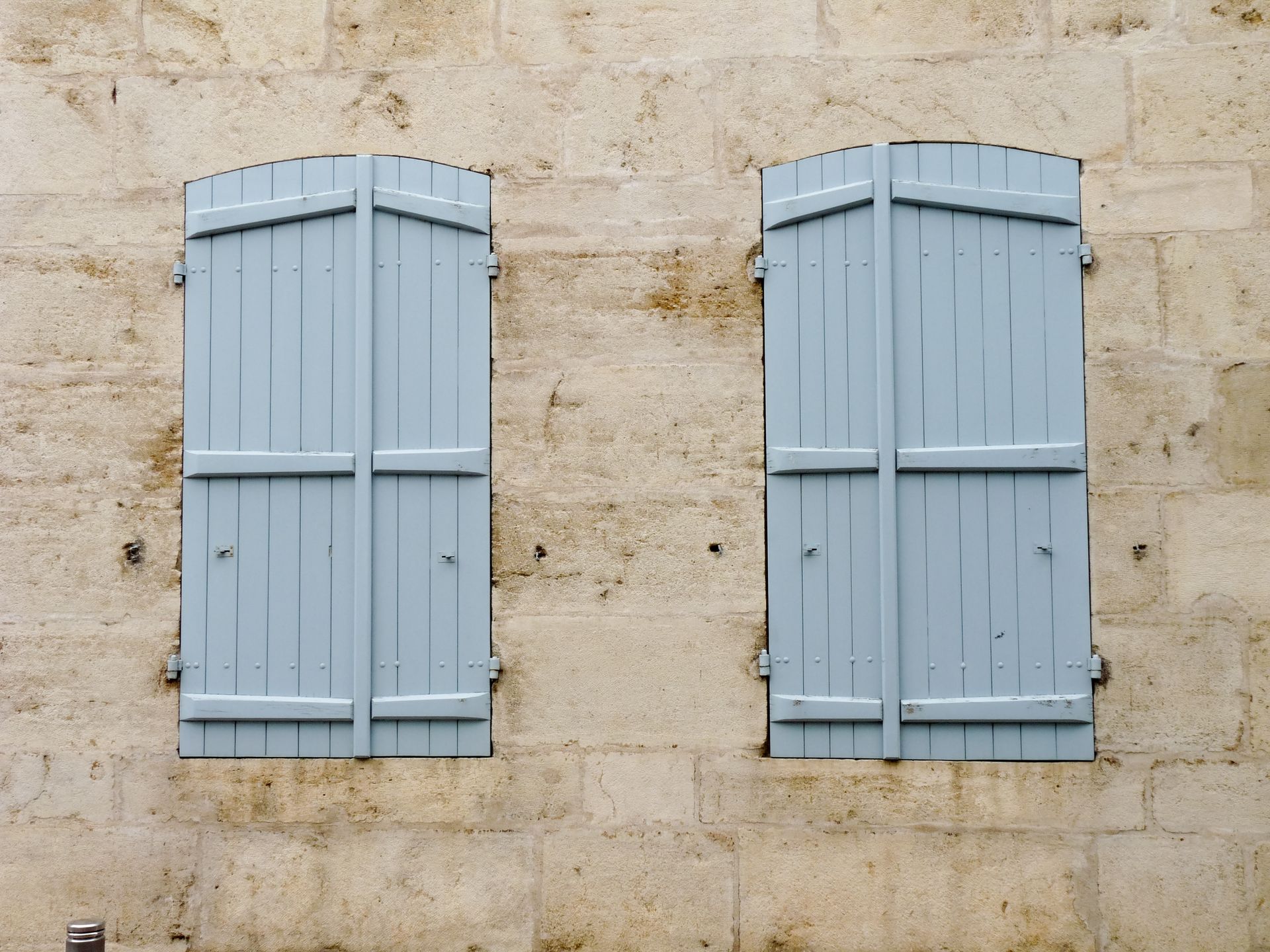 Deux volets bleu clair sur un mur en pierre beige texturée.