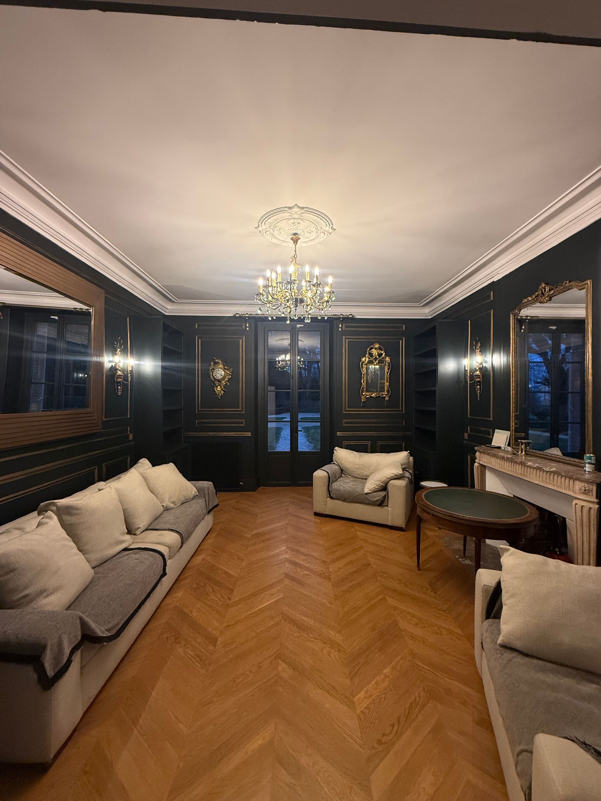 Salon luxueux avec murs lambrissés noirs, parquet et lustre orné.