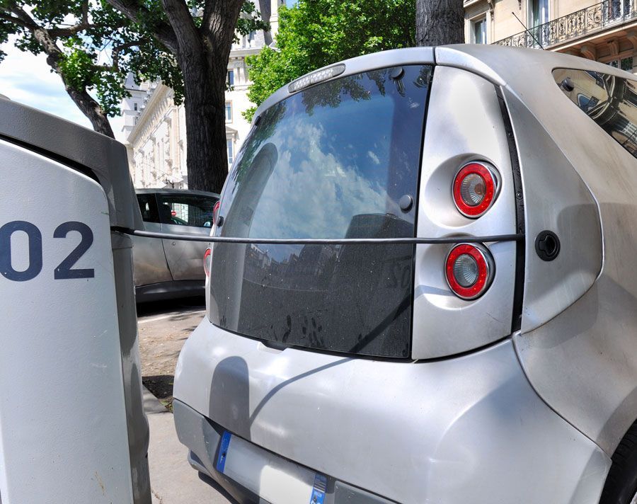 Voiture électrique argentée garée à côté d'une borne de recharge en milieu urbain.