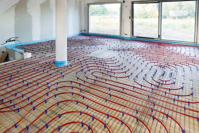 Tuyaux rouges d'un système de chauffage au sol radiant installé sur un plancher en bois dans une pièce avec fenêtres.