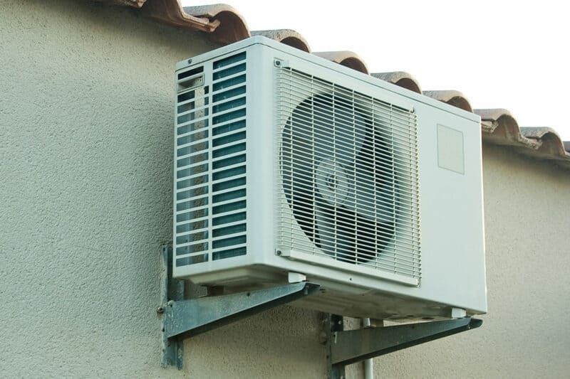 Un climatiseur installé sur la façade beige d'un bâtiment.