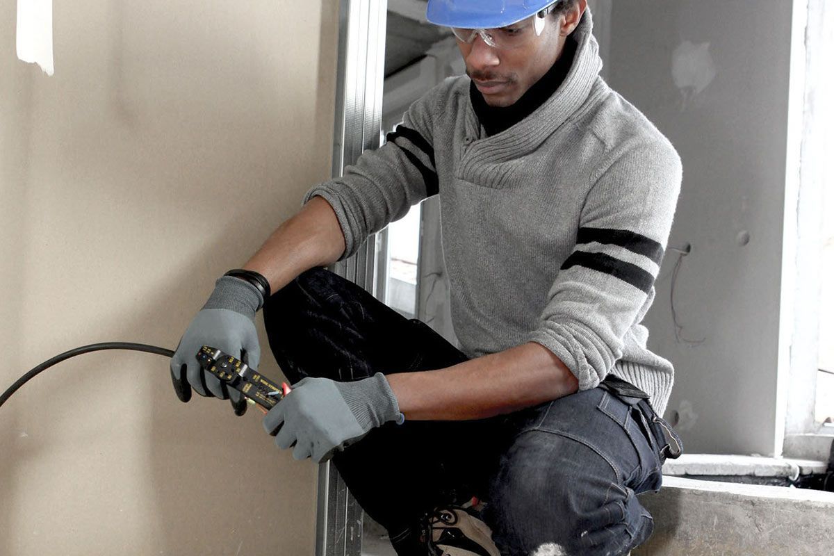 Personne portant des gants et un casque de chantier, coupant un câble sur un chantier de construction.