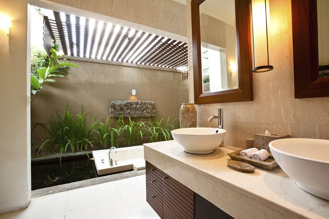 Salle de bains avec douche à l'italienne ; lavabos blancs, meubles en bois, verdure et palette de couleurs neutres.
