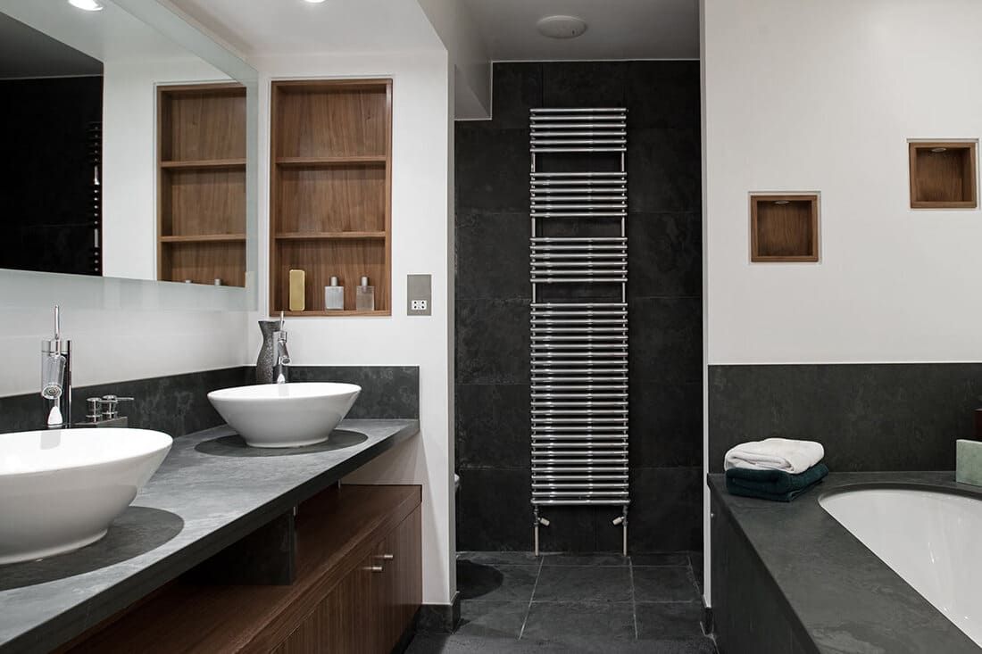 Salle de bains moderne avec carrelage foncé, deux vasques, un porte-serviettes chauffant et des étagères encastrées.