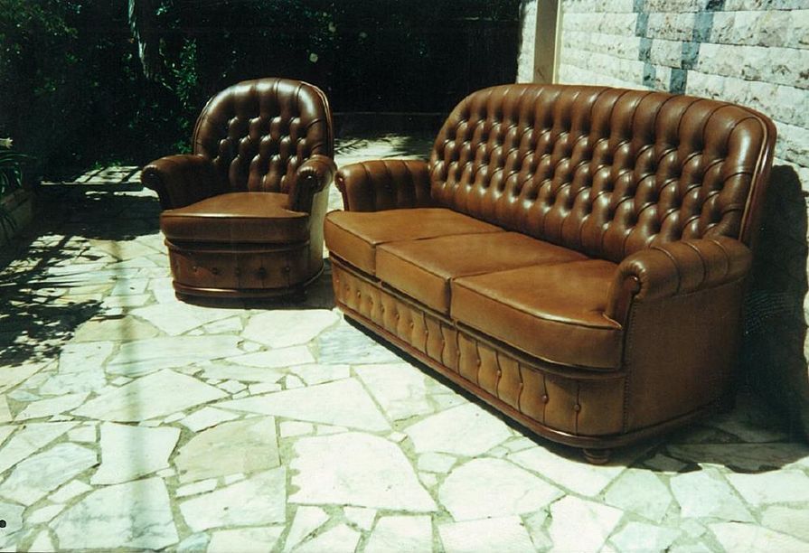 Conjunto de sofá e poltrona de couro marrom em um pátio de pedra, ao ar livre.