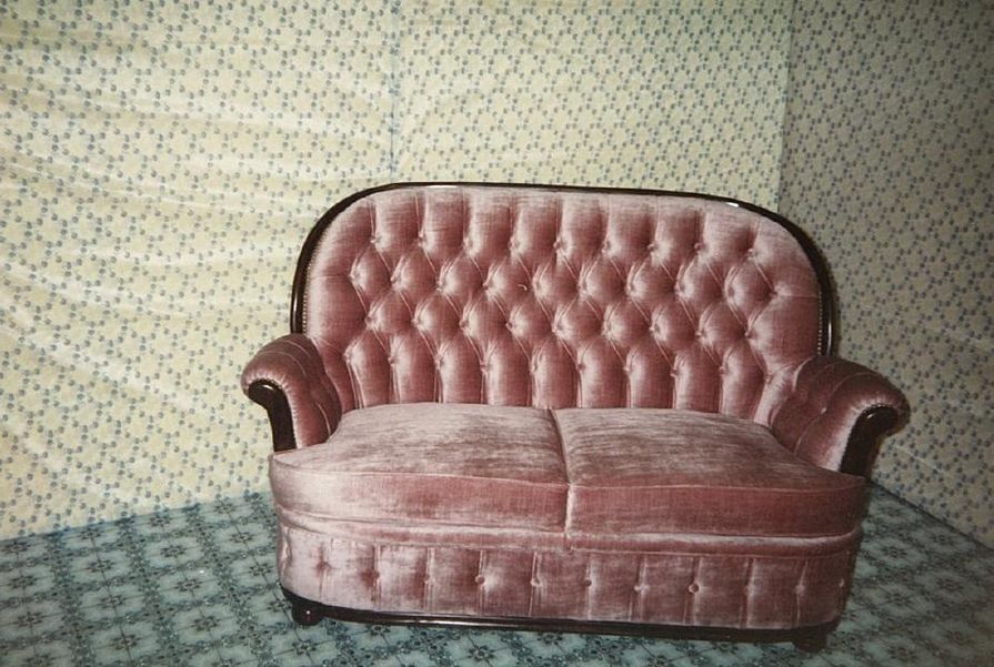 Sofá de veludo rosa com papel de parede e piso estampados.