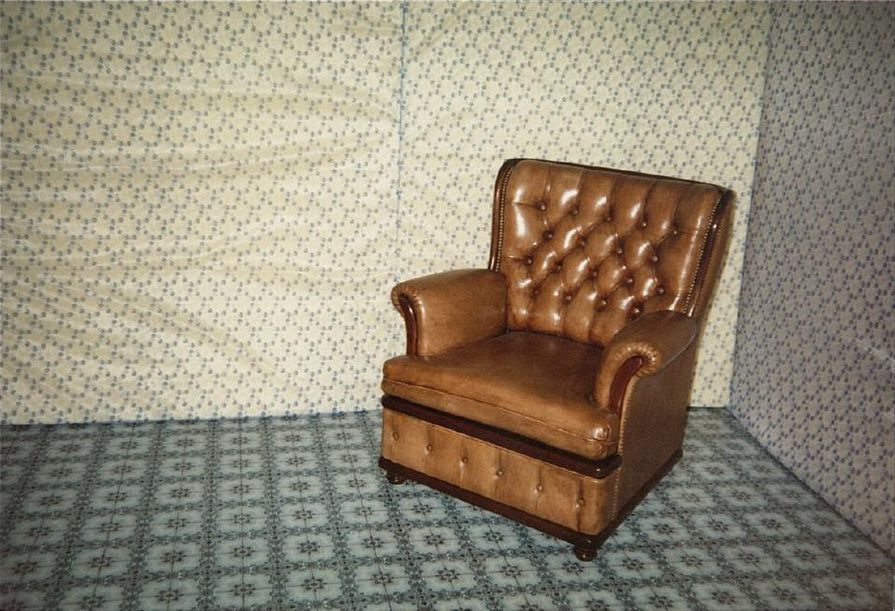 Poltrona de couro marrom em uma sala com papel de parede estampado e carpete.