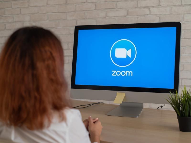 Persona frente a un monitor de escritorio que muestra el logotipo de Zoom en un entorno de oficina en casa.