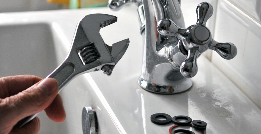 Main tenant une clé près d'un lavabo de salle de bain, réparant peut-être un robinet.