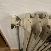 Radiateur blanc contre un mur blanc, avec une valve noire.