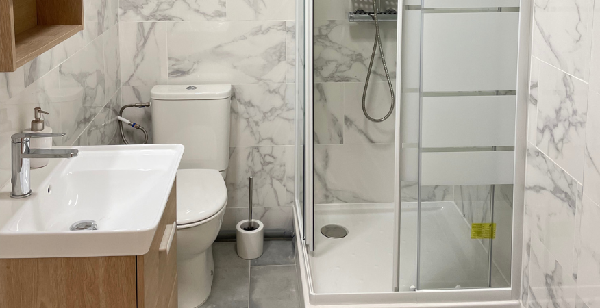 Salle de bain avec murs effet marbre, toilettes, lavabo et porte de douche en verre.