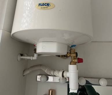 Un chauffe-eau blanc, « FLECK », avec des vannes rouges et bleues, monté sur un mur.