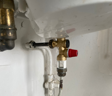 Vanne en laiton raccordée à un chauffe-eau blanc. Soupape de surpression rouge et voyant transparent visibles.
