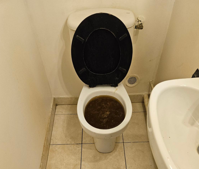 Toilettes remplies d'eau brune, à côté d'un bidet blanc, situées dans une salle de bain carrelée.