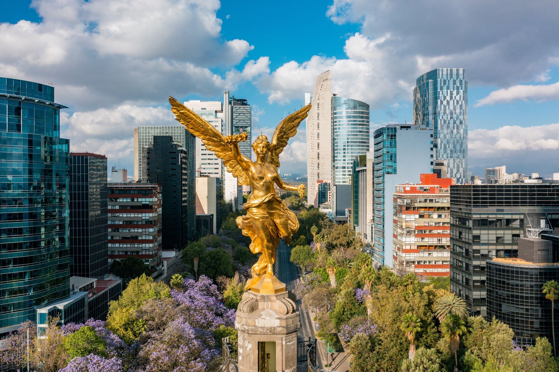 Golden Angel of Independence statue in Mexico City, surrounded by tall buildings and a bright blue sky.