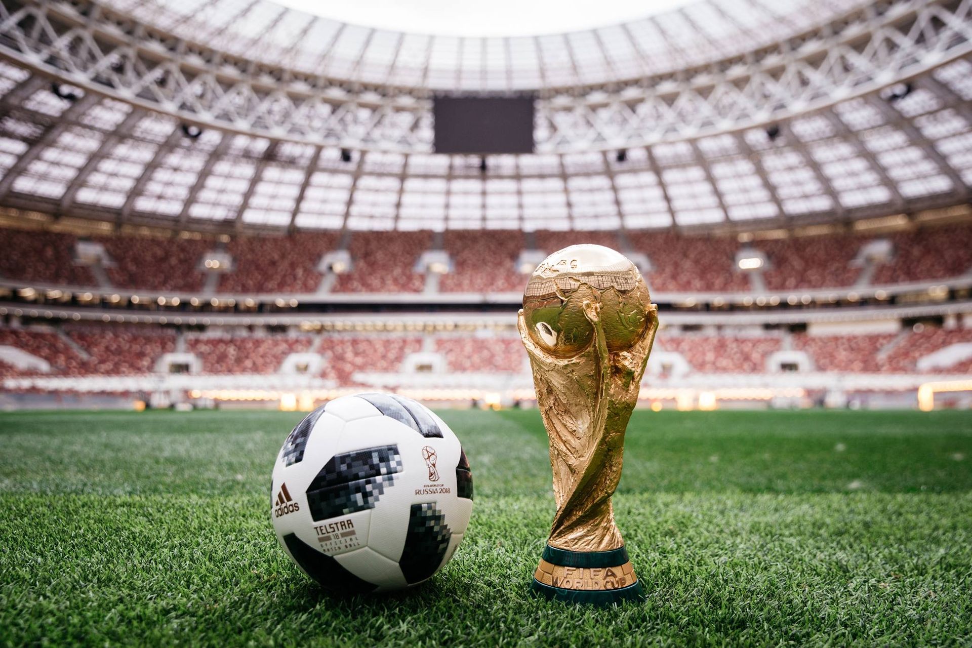 Soccer ball and World Cup trophy on green field in a stadium.