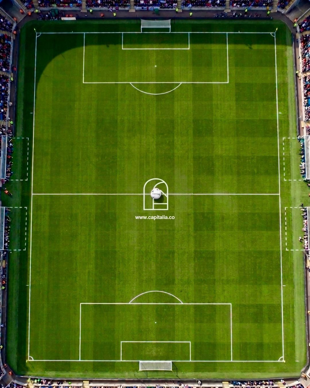 Aerial view of a lit soccer field with white markings and green striped grass at night.