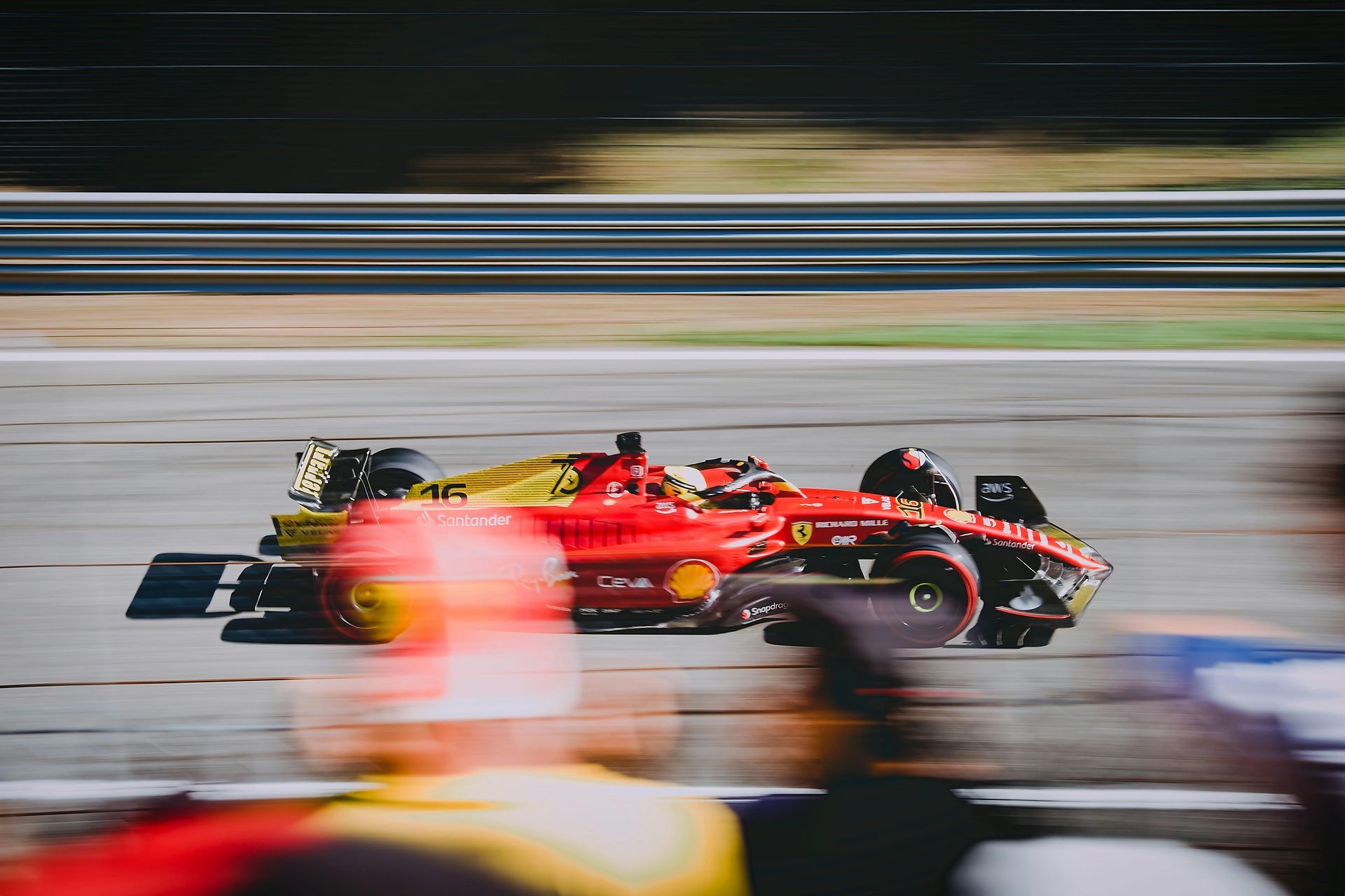 Red and yellow Formula 1 race car speeding on a track, blurred background of spectators and track.
