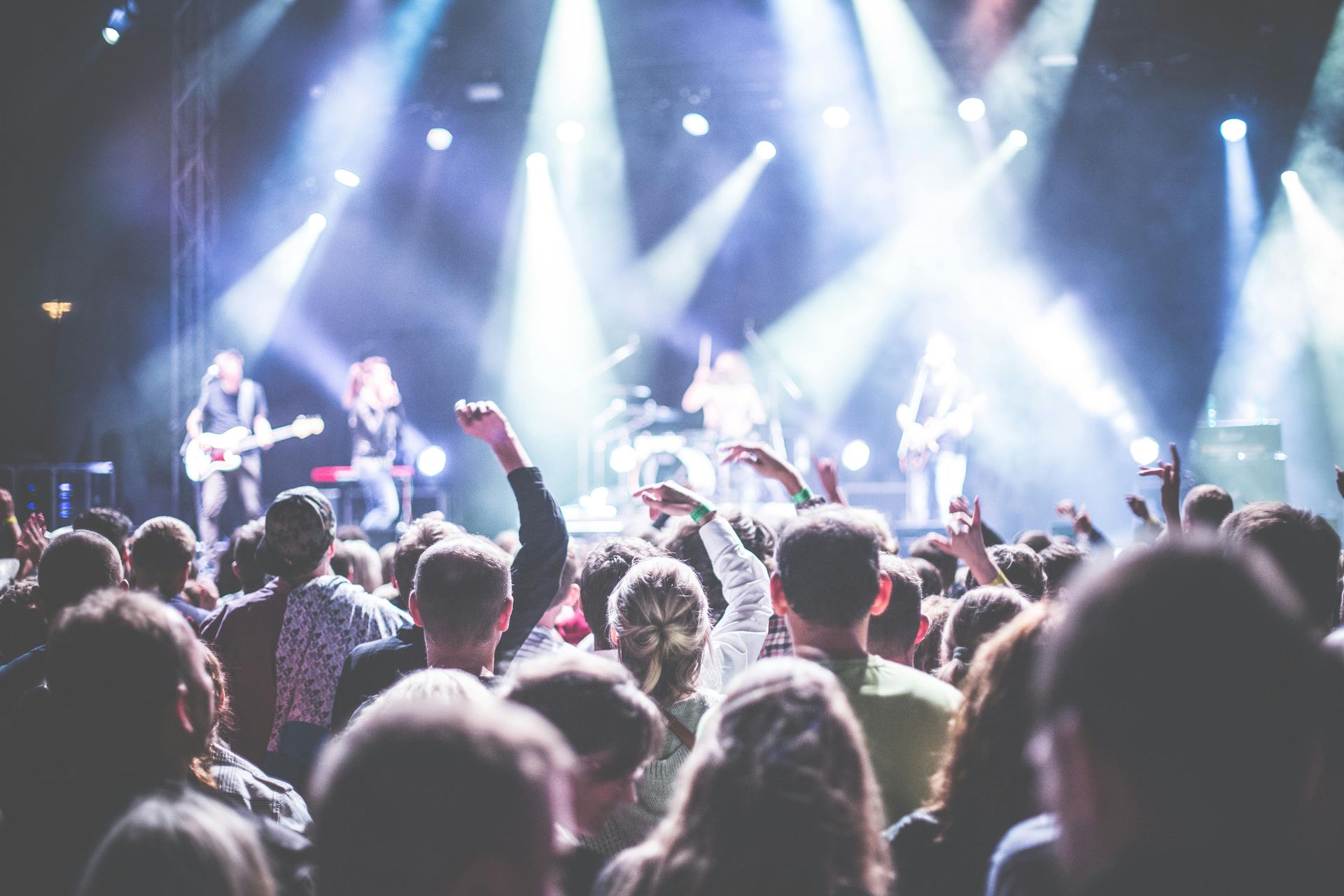 Crowd at a live concert with bright stage lights and band performing in the background