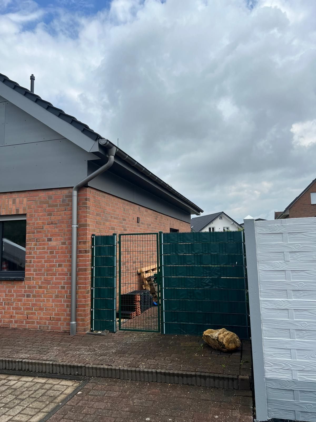 Ein Backsteinhaus mit einem grünen Zaun davor.