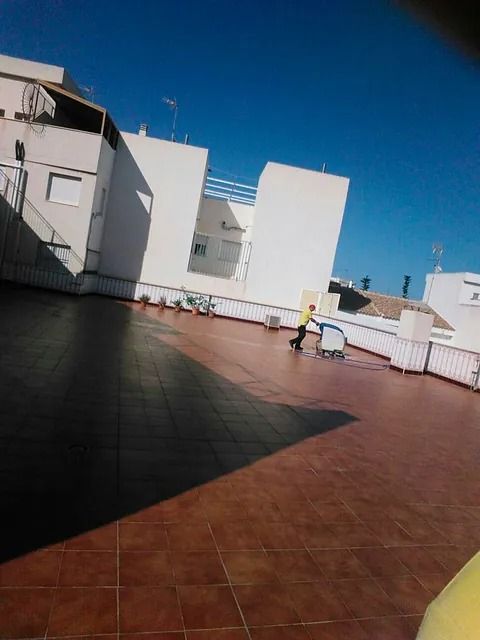 Persona que utiliza una máquina de limpieza en un tejado de tejas, edificios blancos, cielo azul.