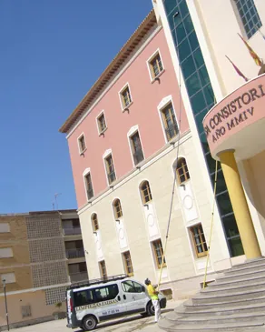 Trabajadores limpiando ventanas de un edificio alto con una camioneta comercial estacionada debajo.