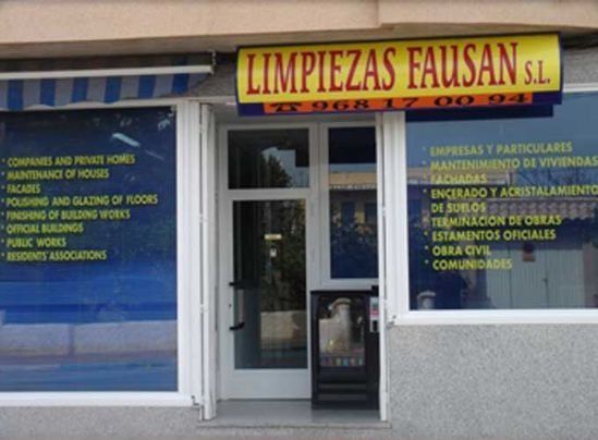 Exterior de oficina del servicio de limpieza Limpiezas Fausan SL, con listados en letras azules en ventanas, toldo de rayas y cartel con número de teléfono.