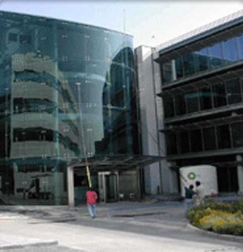 Moderno edificio de oficinas de cristal con gente caminando y una entrada parcialmente oscurecida.