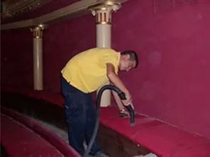 Persona aspirando un asiento rojo en un teatro, columnas al fondo.