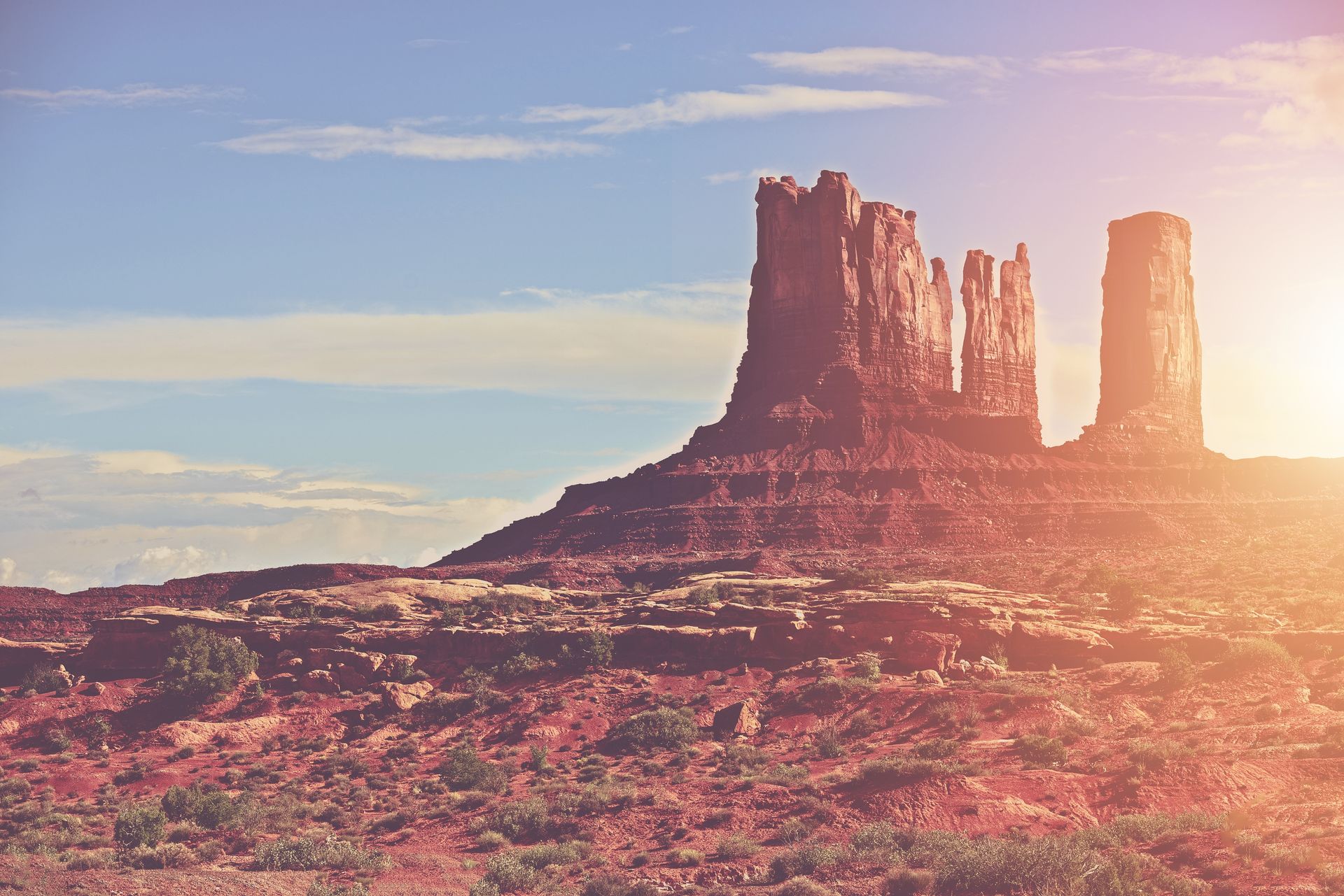 A desert landscape with a mountain in the background and the sun shining through the clouds.
