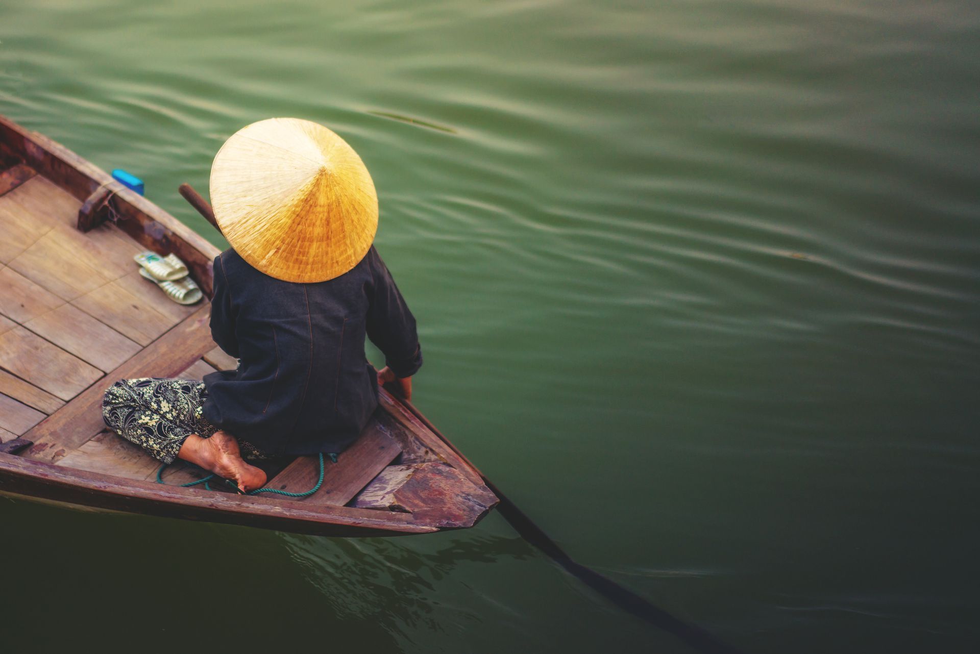 A woman wearing a conical hat is rowing a boat in the water.