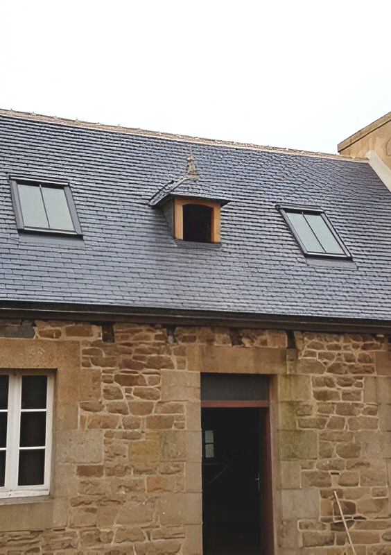 Bâtiment en pierre avec toiture en ardoise, puits de lumière et lucarne.