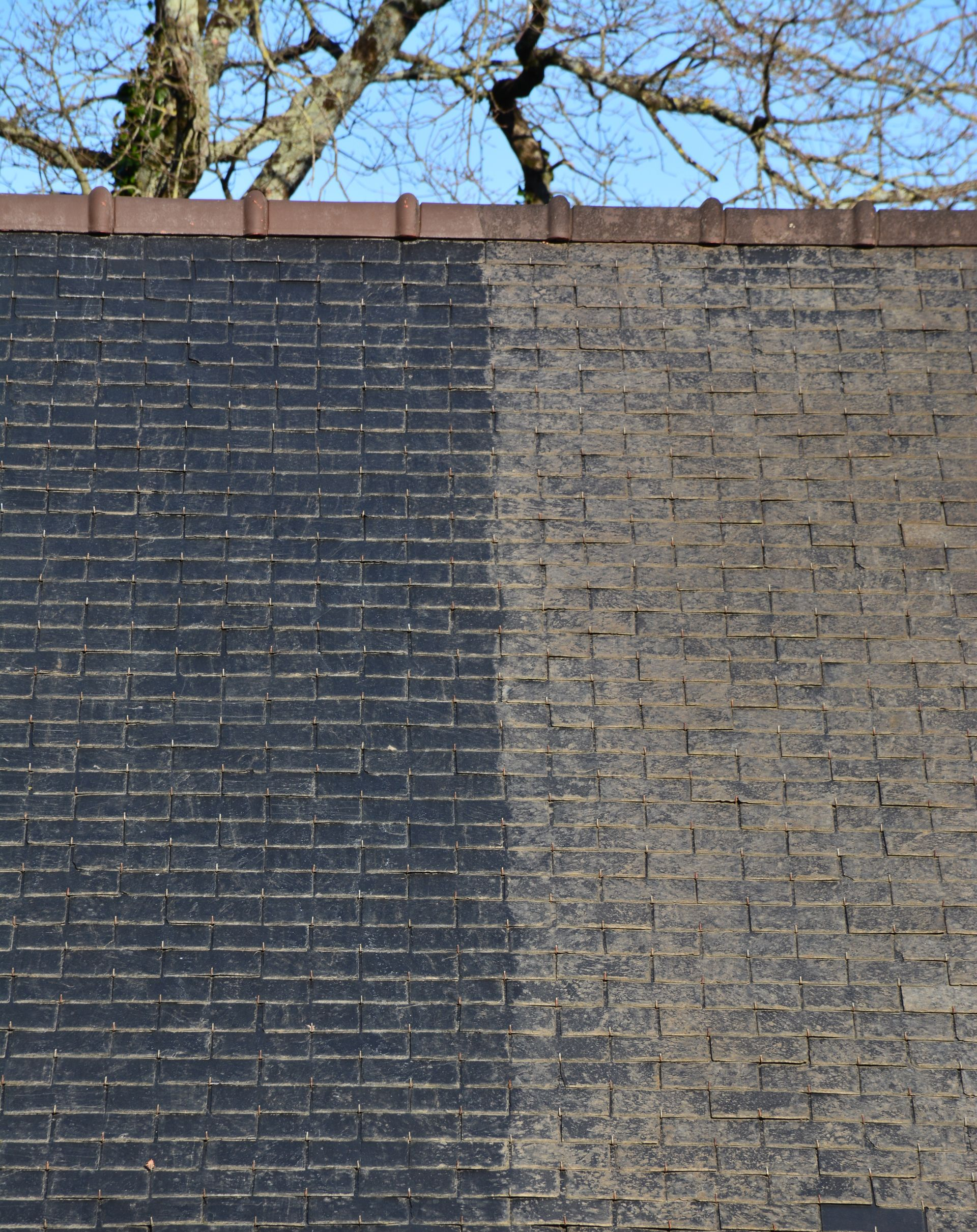 Mur de briques noir et gris montrant une section propre par rapport à une section sale après le nettoyage.