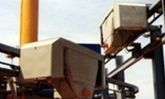 Maquinaria industrial con tolvas y tuberías metálicas contra el cielo.