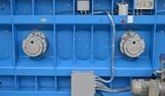 Panel de control industrial azul con dos componentes redondos plateados y una pequeña caja de control gris.
