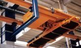 Grúa puente industrial naranja con vigas de soporte azules en el techo de un almacén.