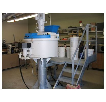 Máquina mezcladora industrial en un taller, con equipo blanco y azul y una plataforma de escalera metálica.