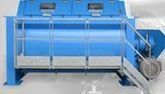 Máquina industrial azul con un gran tanque cilíndrico, estructura metálica y escalera a la derecha.