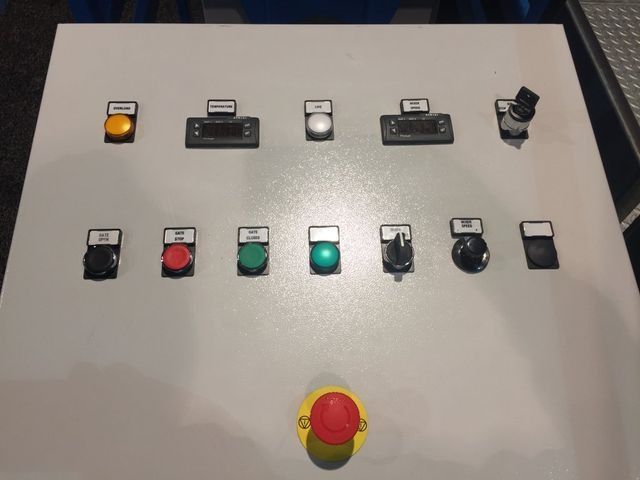 Panel de control con interruptores de palanca y botones, incluido un gran botón rojo de parada de emergencia.
