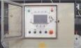 Panel de control industrial montado en la pared con una pequeña pantalla, botones y luces indicadoras contra una pared de hormigón.
