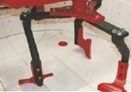 Una máquina de metal rojo y negro se alza sobre un suelo blanco con un agujero circular en el centro.