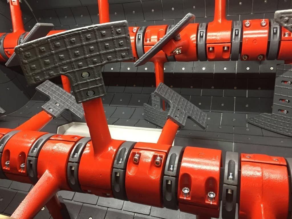 Tuberías y abrazaderas industriales rojas con soportes de metal negro en un entorno de maquinaria.