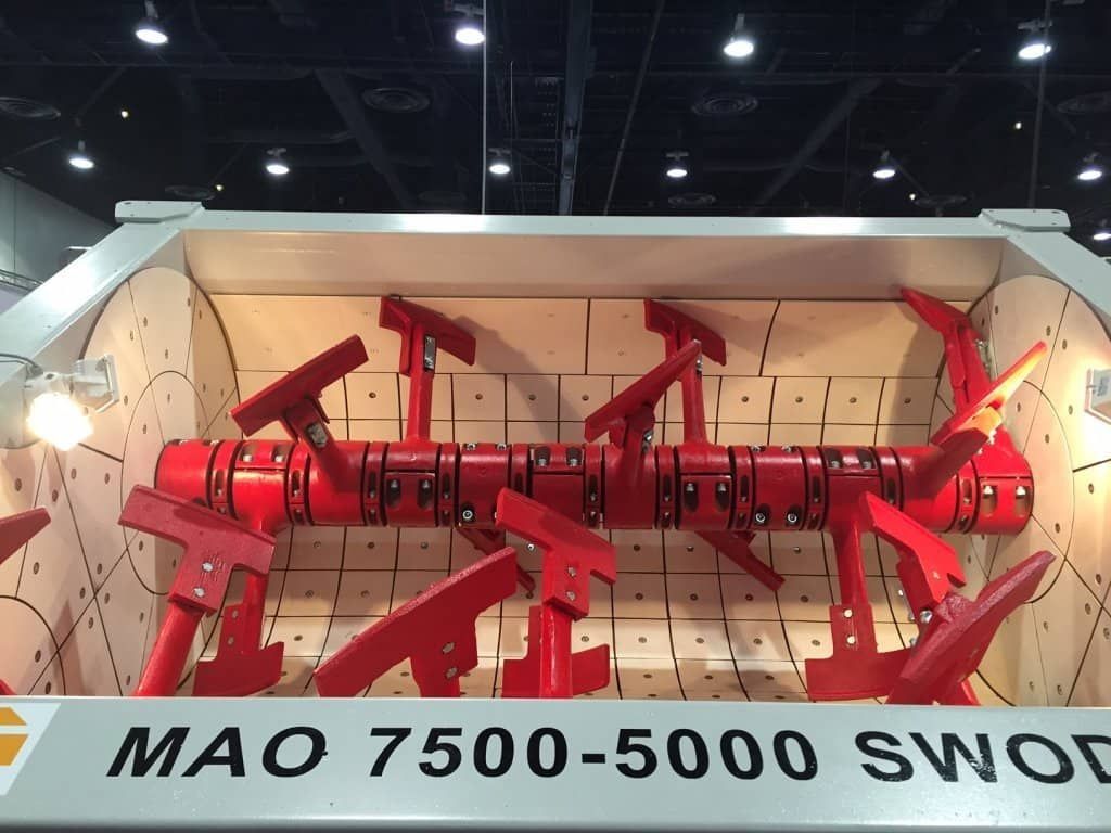 Máquina agrícola roja con múltiples cuchillas expuesta en una sala de exhibición, etiquetada como “MAO 7500-5000 SWO”.