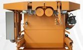 Máquina industrial naranja con mangueras, manómetros y una cubierta superior sobre un fondo blanco.