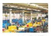 Planta de producción industrial con maquinaria azul y amarilla bajo luces cenitales.