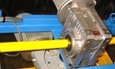 Eje amarillo conectado a una caja de engranajes de metal plateado en maquinaria azul.