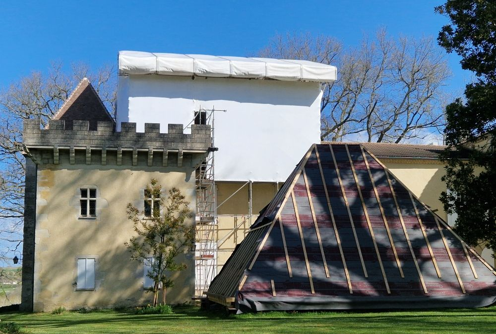 Château en construction, avec échafaudages, bâches et charpente apparente.